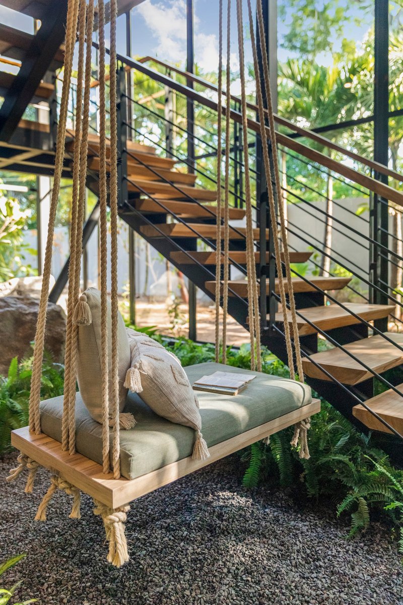 Rope-suspended swing beneath an open-tread steel and timber staircase with ferns