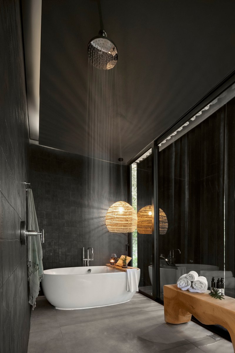 Dark tiled bathroom with freestanding tub under rainfall showerhead and woven pendant light