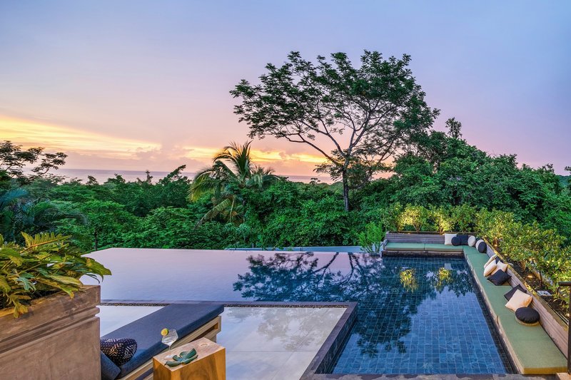 Infinity pool terrace with dark tile mosaic and lounge seating overlooking tropical canopy at dusk