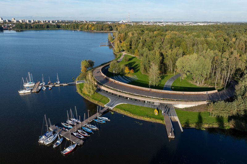 Aerial view of the curving elevated boardwalk with timber slat balustrade between marina docks and forested shoreline