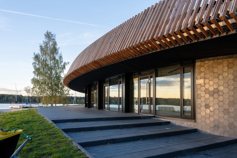 Glass entrance doors reflecting sunset sky beneath the overhanging timber slat roof canopy