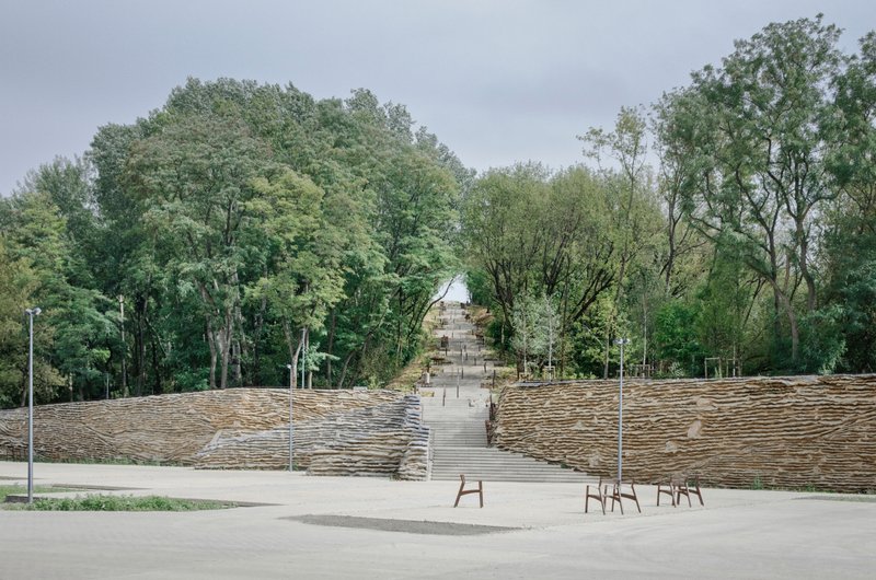 Outdoor amphitheater with timber-stepped seating banks flanking a central staircase under an overcast sky