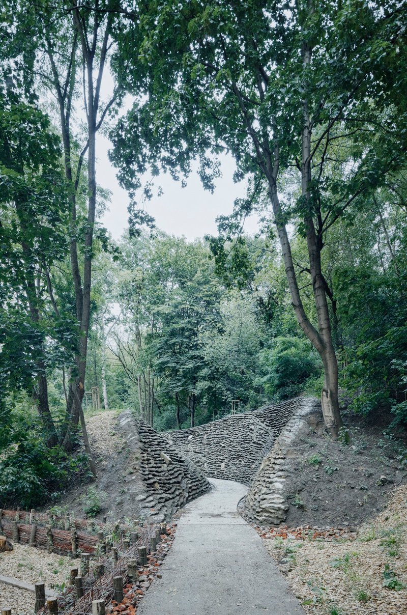 Concrete pathway ascending between layered stone retaining walls in a wooded ravine