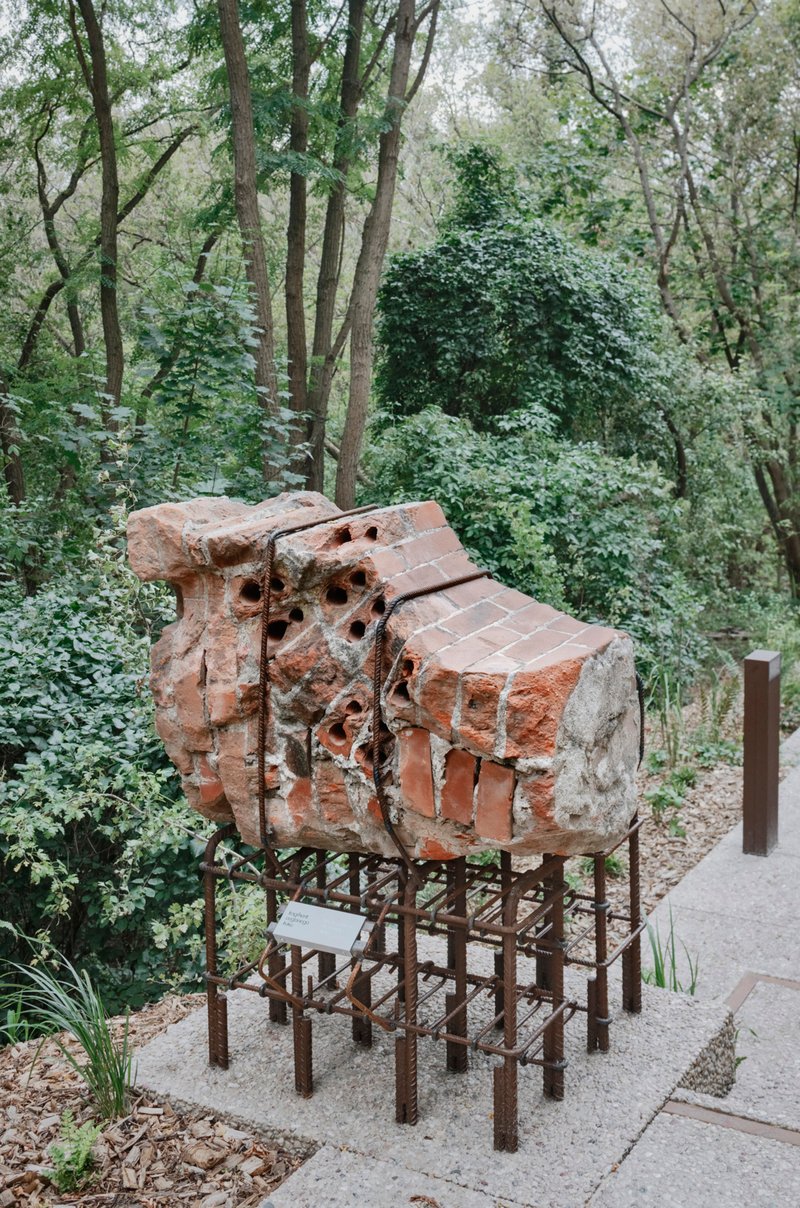 Brick kiln fragment displayed on a steel rebar armature beside a forest path