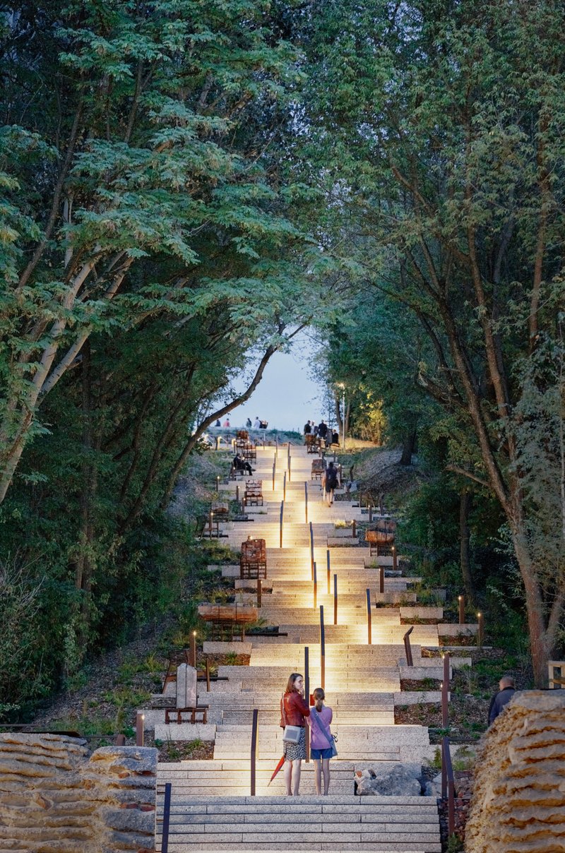 Illuminated stone stairway ascending through a canopy of trees at dusk with visitors scattered along the path