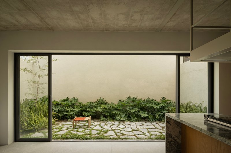 Kitchen view through sliding glass doors to stone-paved courtyard garden with low planted beds