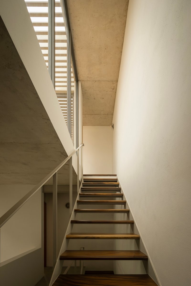 Stairwell with open timber treads and steel stringers ascending beneath a concrete soffit and skylight