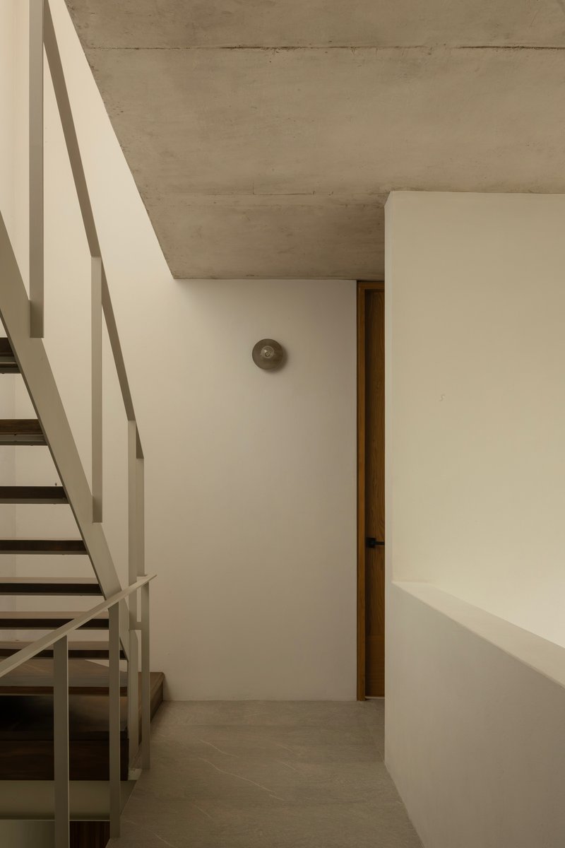 Interior corner showing metal staircase with white railings beneath board-formed concrete ceiling