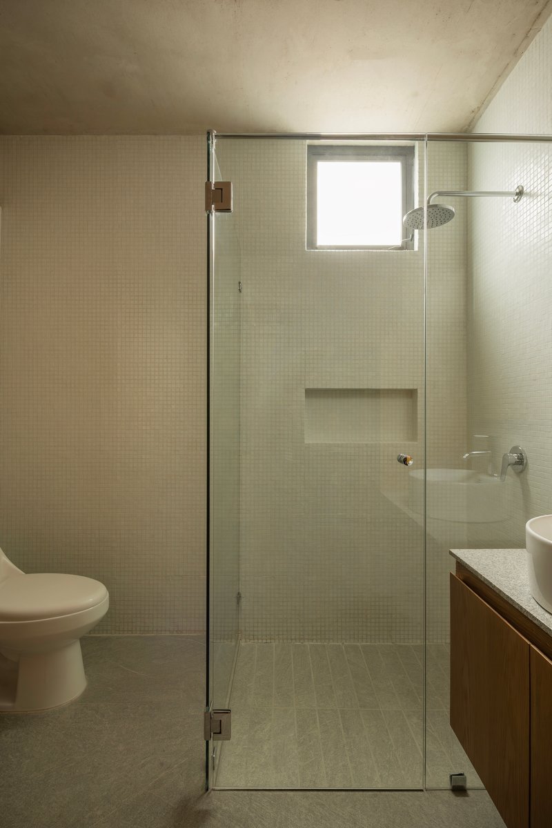 Bathroom with small mosaic tiles, glass shower enclosure and recessed concrete ceiling