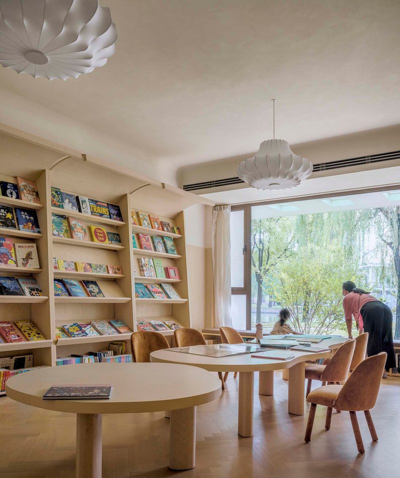 Reading room with built-in bookshelves and round tables beneath pendant lights overlooking the garden
