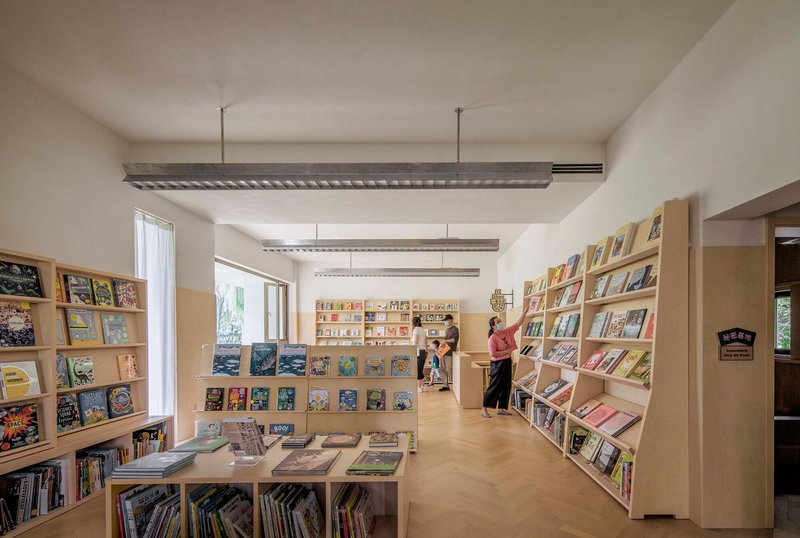 Interior view of library with plywood bookshelves and exposed ceiling beams with visitors browsing books