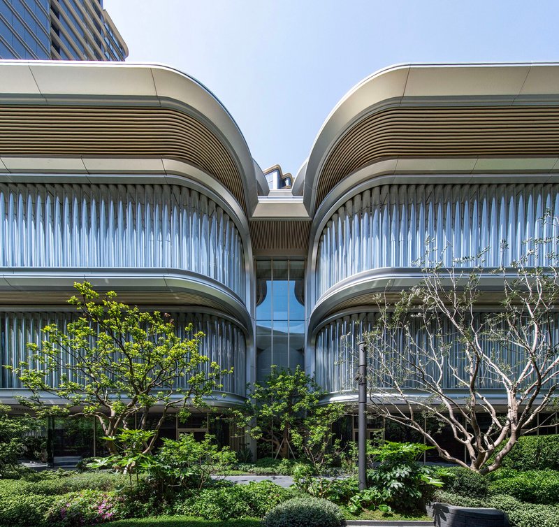 Paired curved volumes with vertical fins and planted terraces framing a glazed entrance under clear blue sky