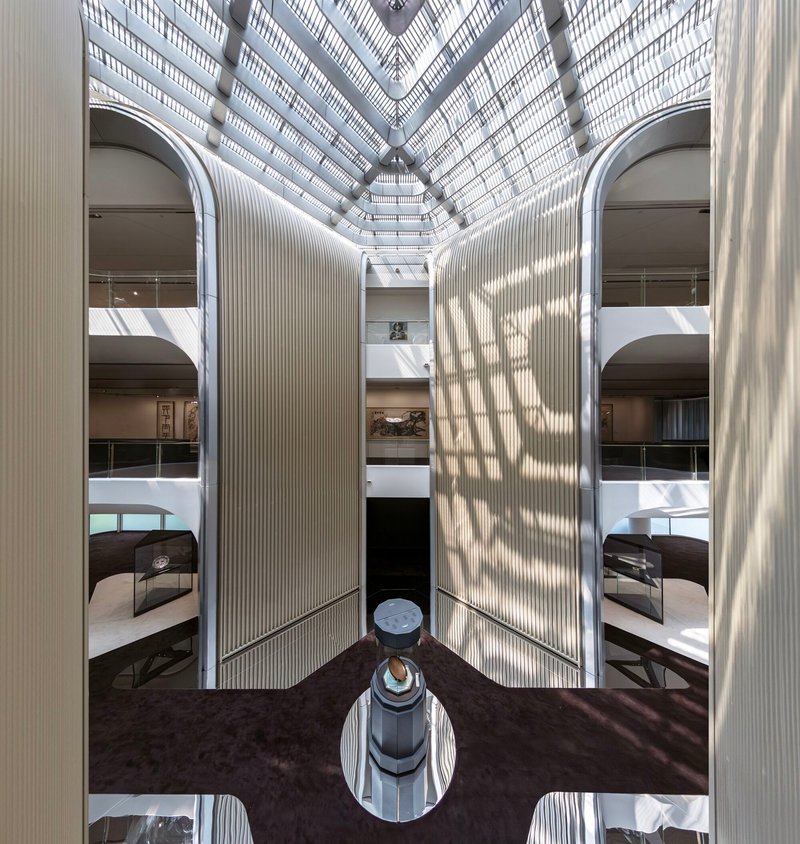 View up a tall atrium showing stacked balconies and vertical ribbed walls converging toward a skylit roof