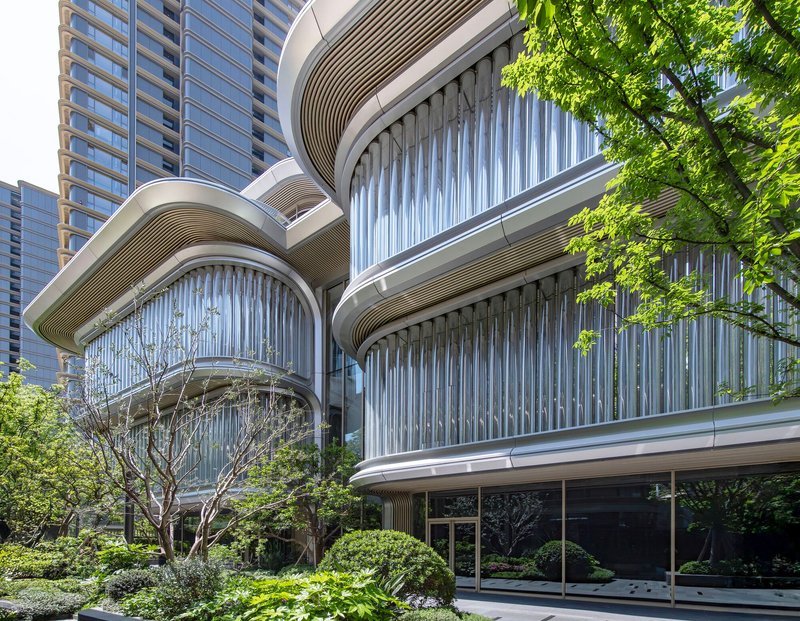 Oblique view of the layered balconies with vertical louvres and curved soffits amid dense foliage in daylight