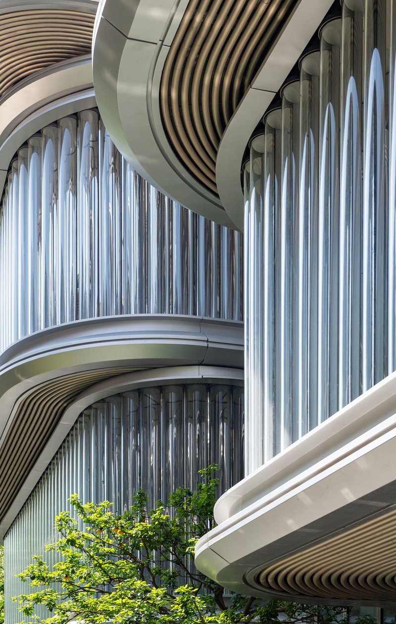Close-up of stacked balconies with white vertical fins and curving soffits beside a tree canopy