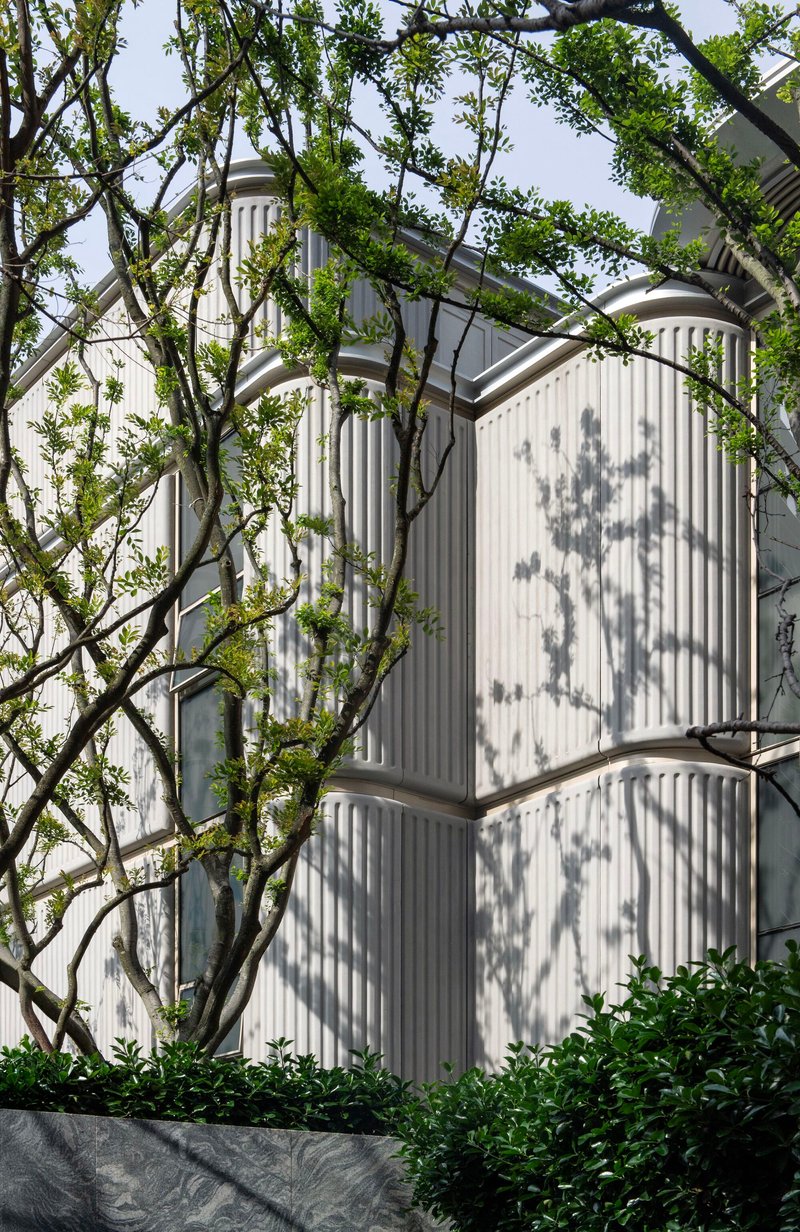 White fluted facade corners with tree shadows cast across the vertical panels and planted bed below