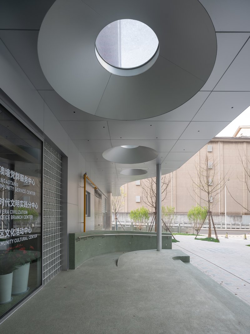 Covered entry plaza with circular skylight, young trees, and glass block wall beside the courtyard