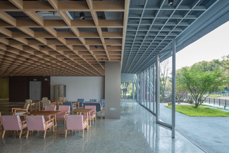 Interior dining area with timber grid ceiling and floor-to-ceiling glass wall overlooking green landscape