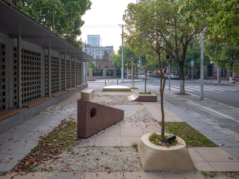 Streetscape view showing perforated facade screen and sculptural concrete benches with circular voids under scattered autumn leaves