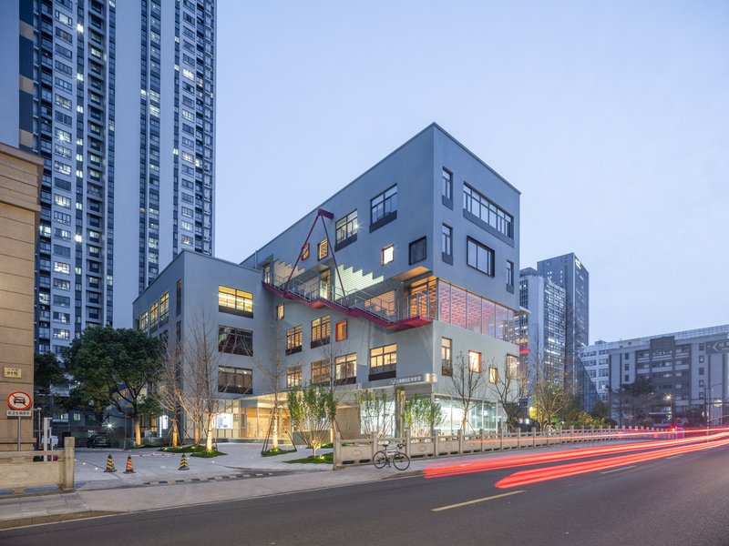 Street view of the stacked volumes with illuminated interiors at dusk and vehicle light trails