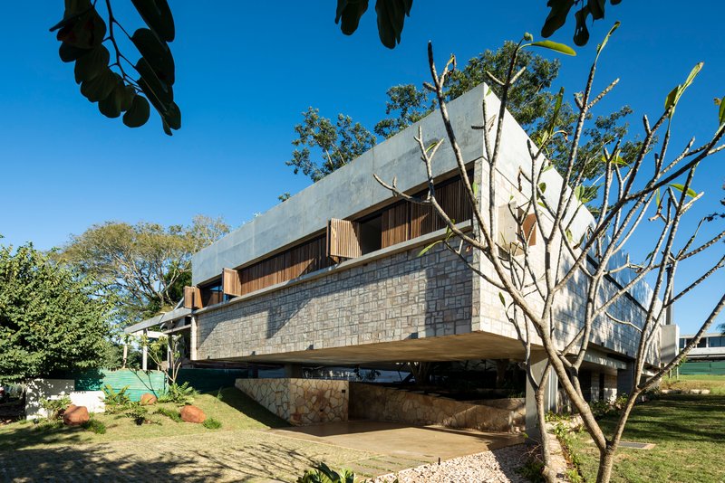 Cantilevered structure supported by concrete pillars with stone cladding and bare trees in foreground
