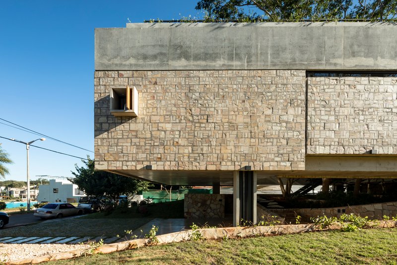 Street view of the stone clad facade with concrete beam and pilotis beneath clear blue sky