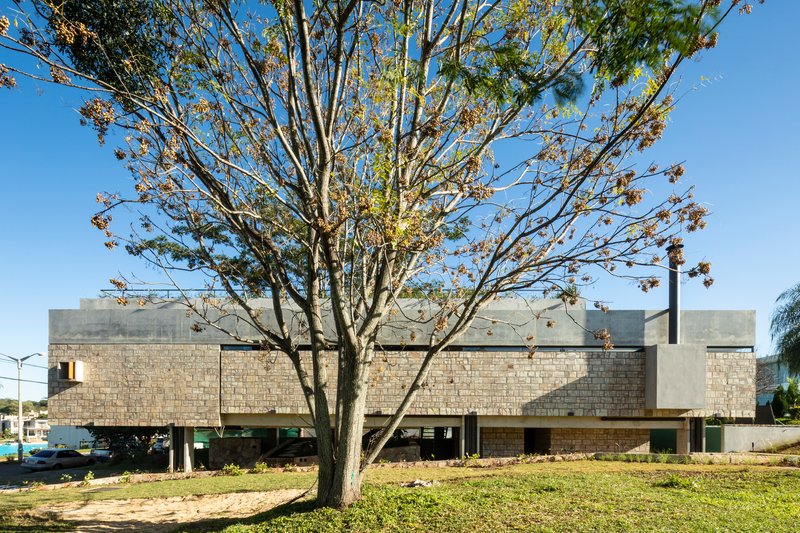 Street view of layered concrete and block facade with bare branching tree in foreground and lawn