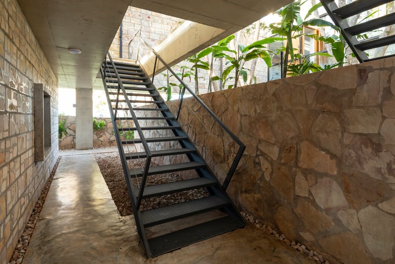 Open steel staircase ascending between stone walls and concrete ceiling with planted courtyard below