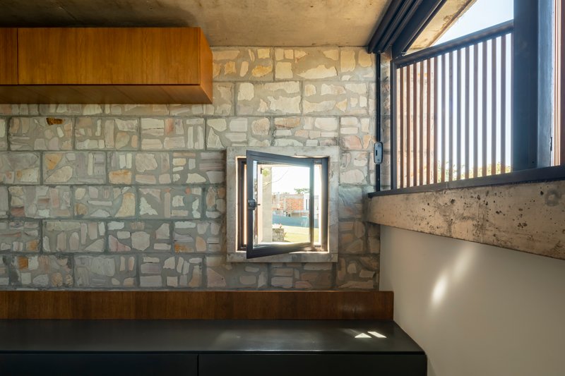 Stone wall with small deep-set window and wooden range hood above dark countertop
