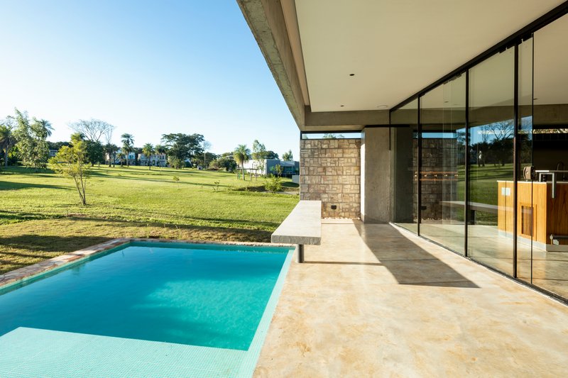 Covered terrace with limestone pavers overlooking a rectangular pool and lawn under clear blue sky
