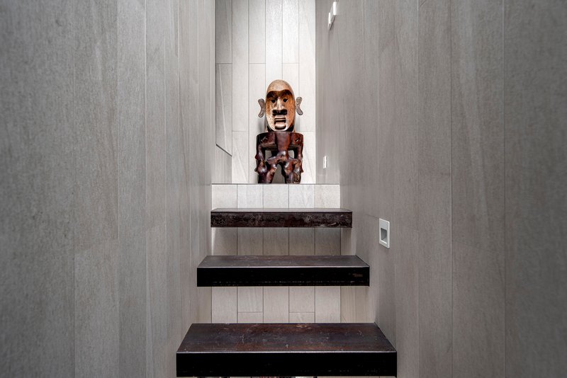 Stairwell with dark cantilevered treads and pale timber wall panels framing a carved mask
