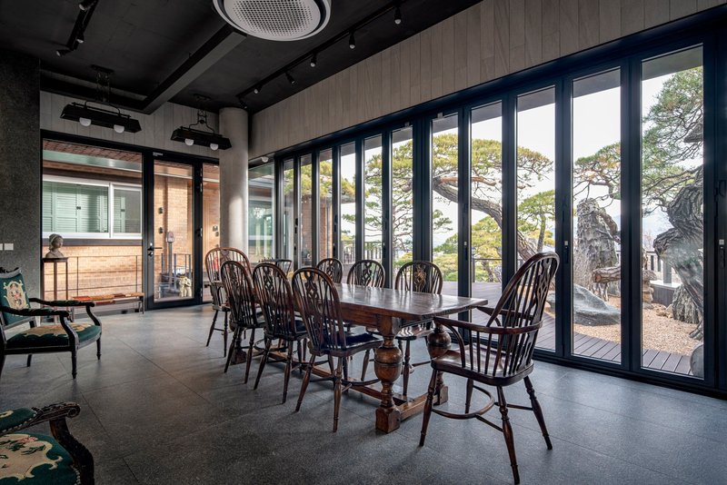 Dining room with full-height glazed wall framing view of pine trees and rock formations outside
