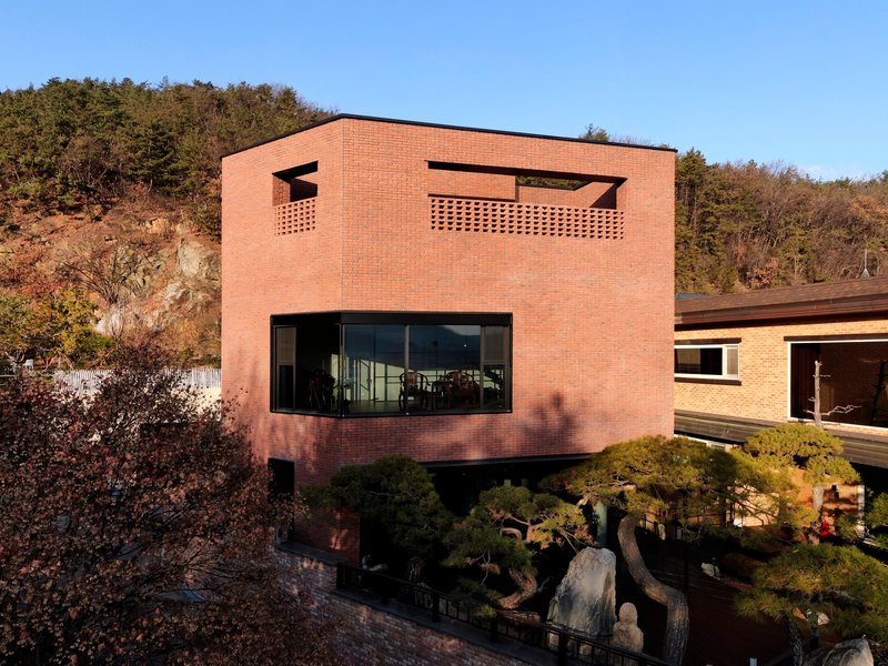 Red brick facade with perforated rooftop parapet and horizontal window band in late afternoon sunlight