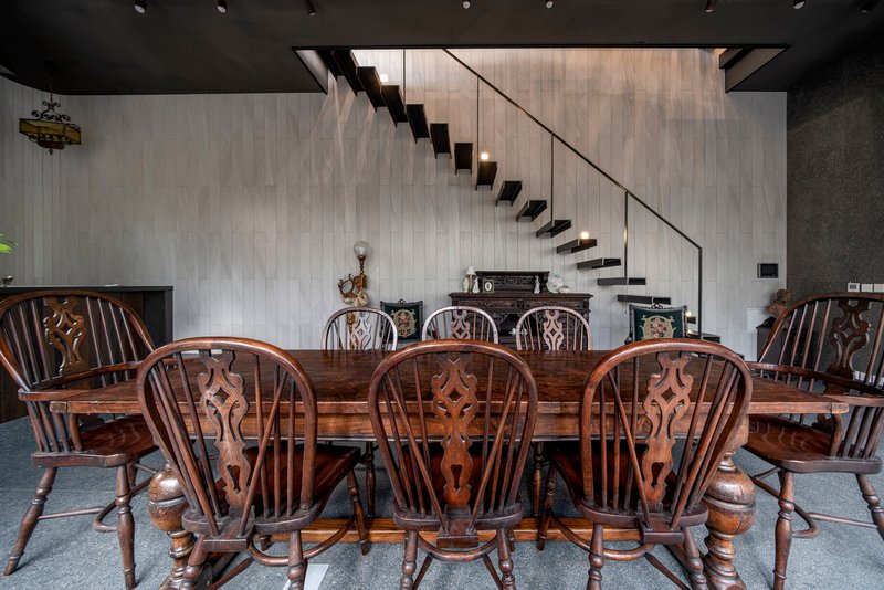 Carved wooden dining chairs arranged around a long table beneath the cantilevered black steel stair