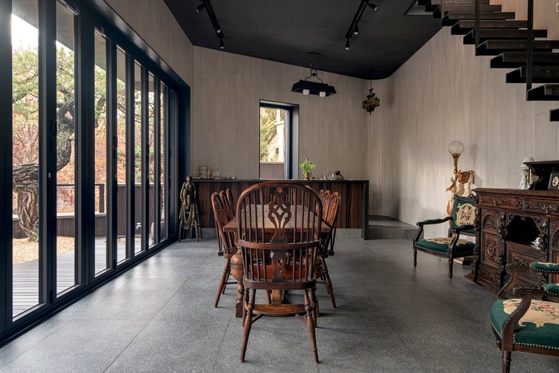 Dining space with tall black-framed glazing overlooking bare trees and a dark ceiling above