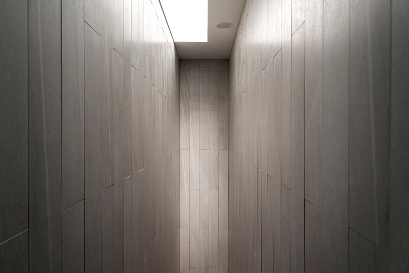 Narrow corridor lined with pale timber paneling and illuminated by a skylight overhead