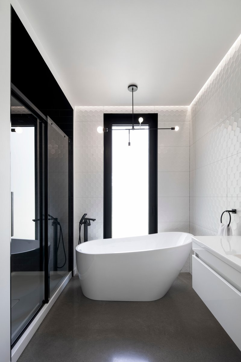 Bathroom with freestanding white tub and concealed perimeter lighting along white tiled walls