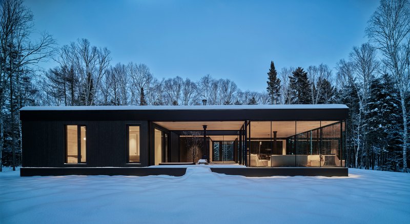 Flat roofed pavilion in deep snow with interior lights glowing under blue twilight