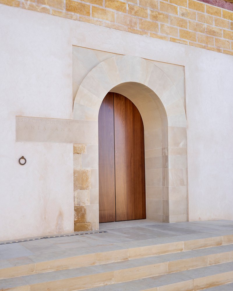 Arched timber entry door framed by limestone voussoirs set within a white stucco facade above stone steps