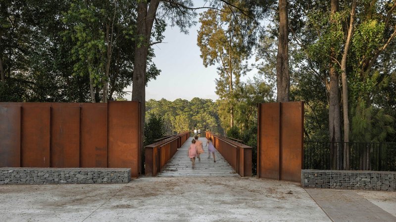 Weathered steel bridge flanked by corten panel walls and gabion retaining walls with visitors walking