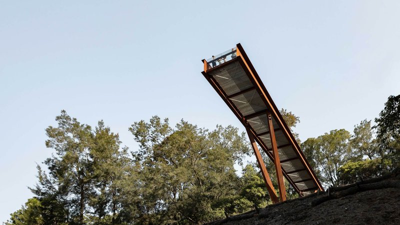 Elevated walkway with weathered steel frame and perforated mesh deck angled against a clear sky