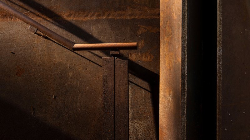 Detail of weathered steel wall panels meeting a handrail in warm afternoon light