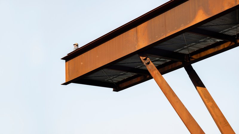 Underside view of the cantilevered steel beam supported by angled weathering steel columns against an overcast sky