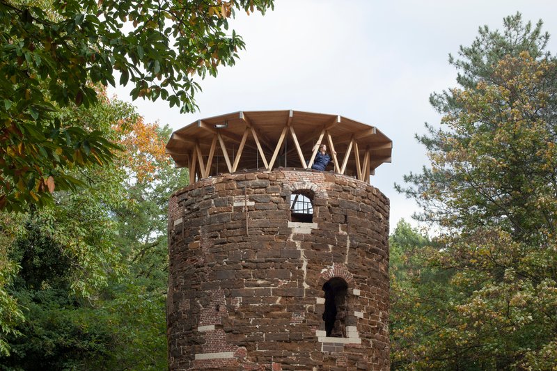 Close view of weathered brick tower with arched openings topped by exposed timber rafters