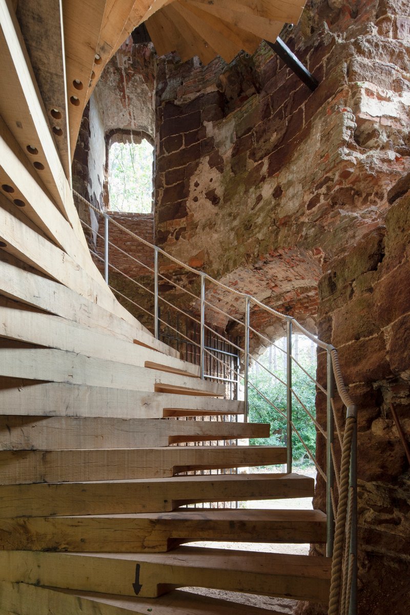 Laminated timber staircase curving along the interior of the deteriorated masonry wall