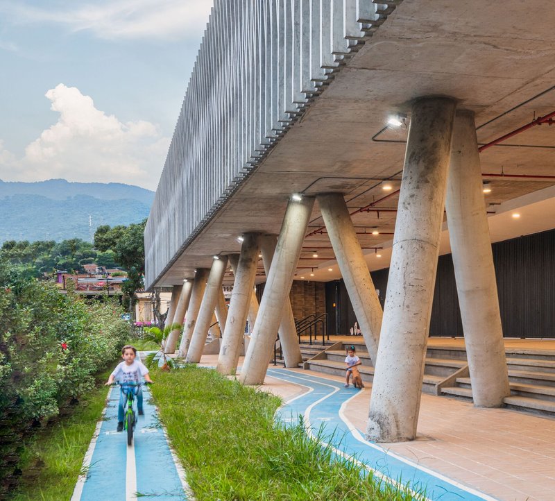 Ground level view of the angled concrete columns, covered walkway, and children on bicycles using the blue path