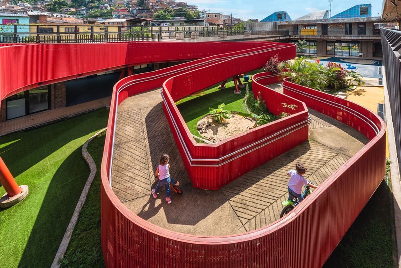 Red corrugated metal walkway curving around planted beds with children walking on paved pathways