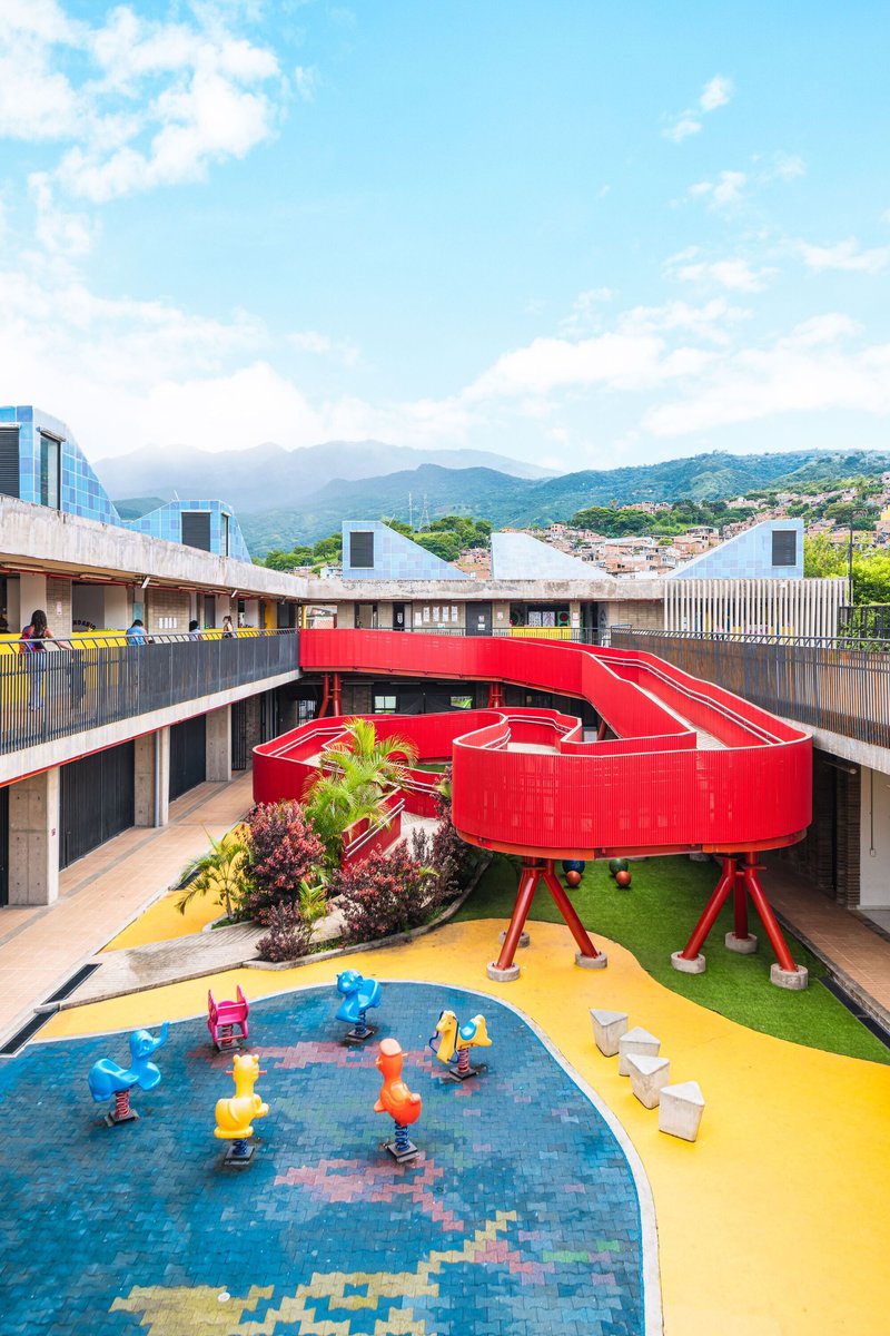 Courtyard with red spiral ramp structure, blue tiled play pool, and yellow surfacing under afternoon clouds