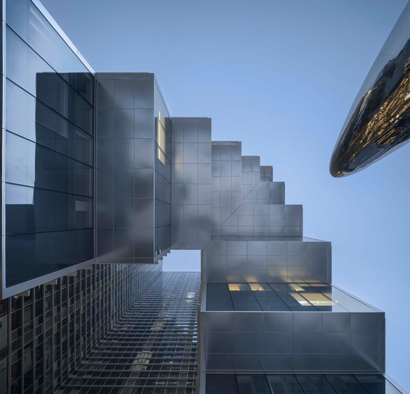 Upward view of the stepped metal panel facade with a glass gridded base at dusk