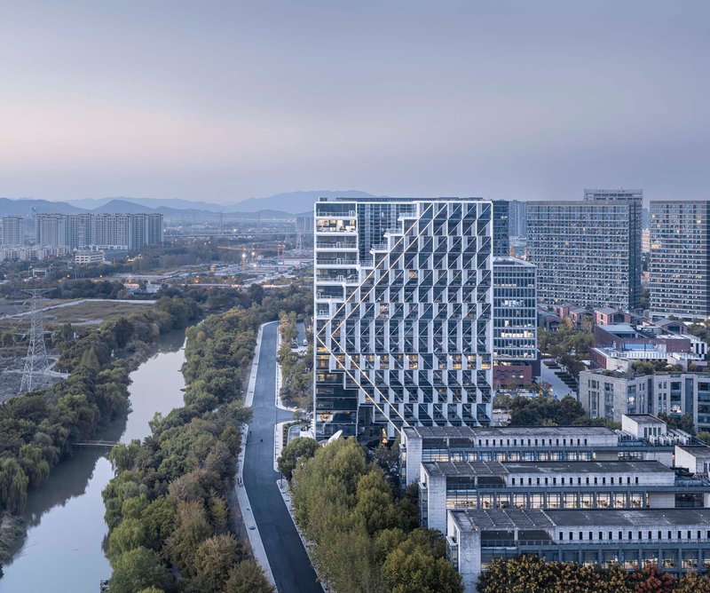 Aerial view of the tower with its patterned glass facade rising above a tree-lined canal at dusk